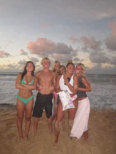 a group of people standing on top of a sandy beach next to the ocean at sunset