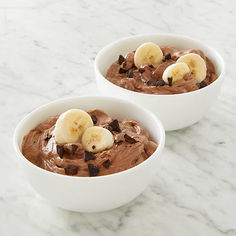 two bowls filled with chocolate pudding and bananas on top of a marble countertop next to each other