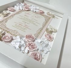 a wedding card with pink and white paper flowers in a shadow box on a table