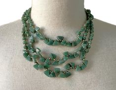 A Lovely Three -Strand Necklace Featuring Celadon Green-Colored Aventurine Beads Triangle Cut and Round Cut Beads with Brass Beads and Brass Twist Clasp The Three Graduated Strands Vary in Length, the Shortest Measuring Approximately 18 inches (44cm) and the Longest Approximately 21 1/2 inches (55cm) The Round Aventurine Beads Measure 5mm in Diameter The Triangle Aventurine Beads Measure 3/8" Long The Total Weight of the Necklace is 100 Grams This is a Very Versatile Necklace - Suitable for Day or Evening New Vintage From the 1980's COMPLIMENTARY DOMESTIC SHIPPING Aventurine Beaded Necklace With Faceted Beads, Elegant Aventurine Beaded Necklaces With Polished Beads, Elegant Aventurine Beaded Necklace With Polished Beads, Three Strand Necklace, Aventurine Necklace, Celadon Green, Brass Beads, The Triangle, Strand Necklace