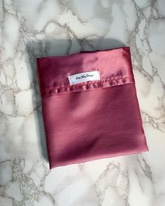 a pink cloth with a label on it sitting on a marble counter top next to a white wall