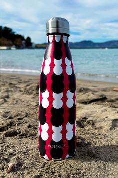 a red and black water bottle sitting on top of a sandy beach