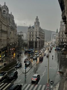 a city street filled with lots of traffic next to tall buildings on a rainy day