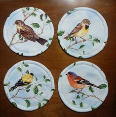 four plates with birds painted on them sitting on a table