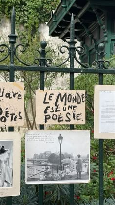 some signs are hanging on a fence near bushes and trees with flowers in the background