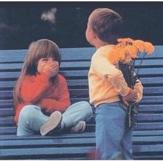 two children sitting on a blue bench and one is covering his mouth while the other holds flowers