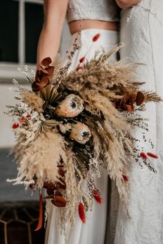 two brides holding bouquets with dried flowers and feathers