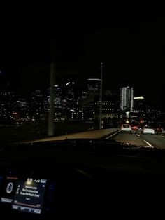 a car driving down a highway at night with the city lights in the back ground