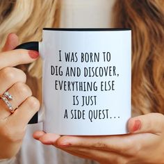 a woman holding a coffee mug with the words i was born to dig and discovery, everything else is just a side quest