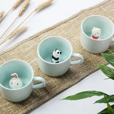 three mugs with small animals in them sitting on a table next to some plants