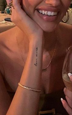 a woman with tattoos on her arm holding a wine glass and smiling at the camera