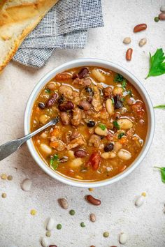 a white bowl filled with beans, meat and bread on top of a table next to some bread