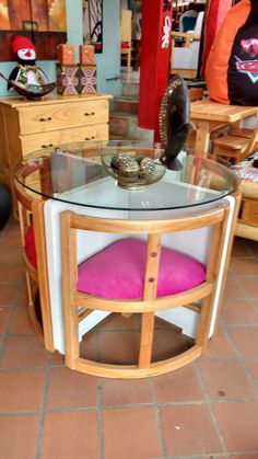 a round glass table with pink cushions in a room filled with wooden furniture and other items