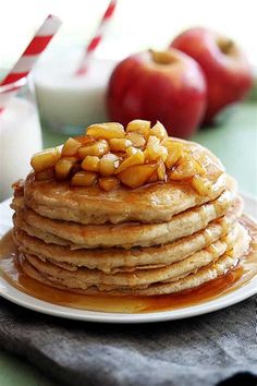 a stack of pancakes covered in syrup and nuts on a plate next to two glasses of milk