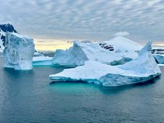 an iceberg floating in the ocean with snow on it's sides and mountains in the background