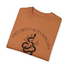 Make a powerful statement with our "They Didn't Burn Witches They Burned Women" Shirt. This thought-provoking tee is perfect for those who appreciate feminist history, embrace their inner strength, and love a touch of nature-inspired design. Features: * The shirt features an impactful quote, "They Didn't Burn Witches They Burned Women," surrounded by an elegant floral and snake illustration. This design pays homage to the courageous women of the Salem Witch Trials and symbolizes resilience and empowerment. * Made from premium Comfort Colors fabric, this shirt offers an incredibly soft and cozy feel, making it a pleasure to wear all day long. * This versatile t-shirt pairs perfectly with jeans, skirts, or leggings, making it a standout piece for any casual outing, protest, or gathering. * W Feminist History, Floral Snake, Snake Illustration, Salem Witch Trials, Snake Lovers, Witch Trials, Salem Witch, Nature Inspired Design, Women Shirt