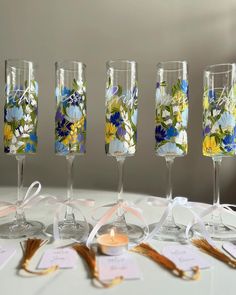 five wine glasses with flowers on them sitting on a table next to tags and candles