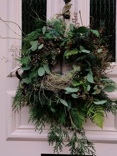 a wreath on the front door of a house with green leaves and greenery hanging from it