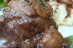 some meat and potatoes on a plate with green leafy greens in the foreground