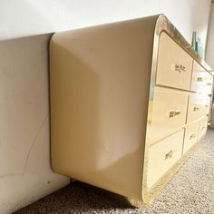 a beige dresser sitting on top of a carpeted floor next to a white wall