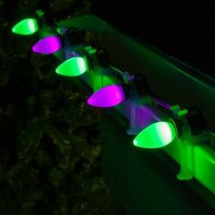 some lights that are sitting on the side of a building in the dark with green and purple colors