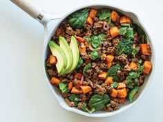 a skillet filled with meat, vegetables and avocado on top of a table