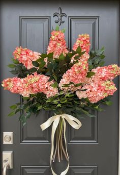 a bouquet of pink flowers is tied to a front door with a bow on it