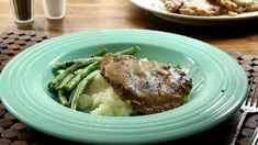 a green plate topped with meat and mashed potatoes next to a glass of water