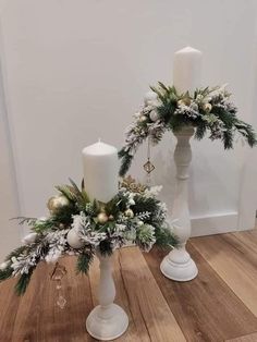 two white candles are sitting next to each other on a wooden floor with greenery