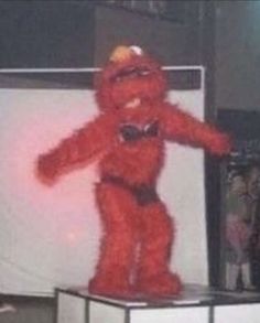 a large red stuffed animal standing on top of a white box in front of a crowd