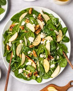 spinach salad with apples and walnuts in a white bowl on a marble table