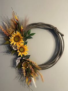 a wreath with sunflowers and feathers hanging on the wall next to a rope