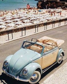 an old car is parked on the side of the road next to the beach with people in the background