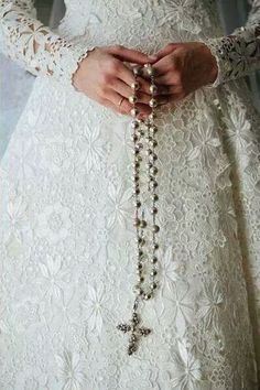 a woman wearing a white dress and holding a rosary