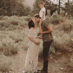 a man and woman kissing while holding a small boy on their shoulders in the middle of a field