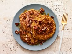 two pancakes with pecans and maple syrup on a blue plate next to a fork