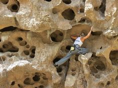 a man climbing up the side of a large rock formation with holes in it's walls