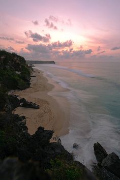 the sun is setting over an ocean with waves crashing on the shore and rocks in the foreground