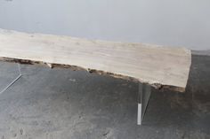 a bench made out of wood and metal legs on concrete floor next to white wall