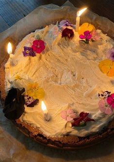 a cake with white frosting and flowers on it, lit by two small candles