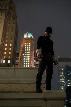 a man standing on top of a building next to tall buildings in the city at night