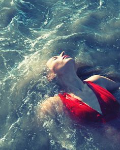 a woman in a red swimsuit floating on top of the ocean with her eyes closed