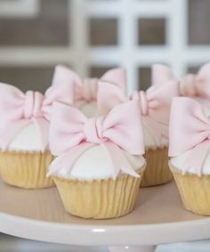 three cupcakes with pink bows are on a cake plate