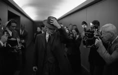 a man in a suit and hat walking down a hallway with cameras around him,