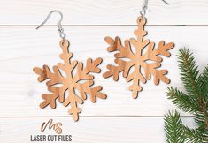 two wooden snowflakes hanging from hooks on a white wood background with pine branches