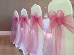 chairs with pink sashes and bows on them are set up for a wedding reception