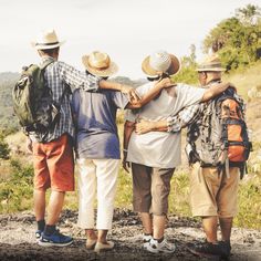 four people standing together with backpacks and hats on their backs, looking at the mountains