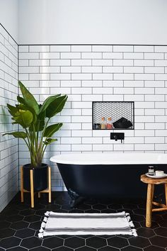 a black and white tiled bathroom with a plant in the bathtub next to it