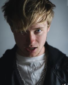 a close up of a person wearing a black jacket and white shirt with a necklace on his neck