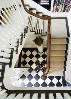 an overhead view of a staircase with black and white checkered flooring, bookshelves and a vase